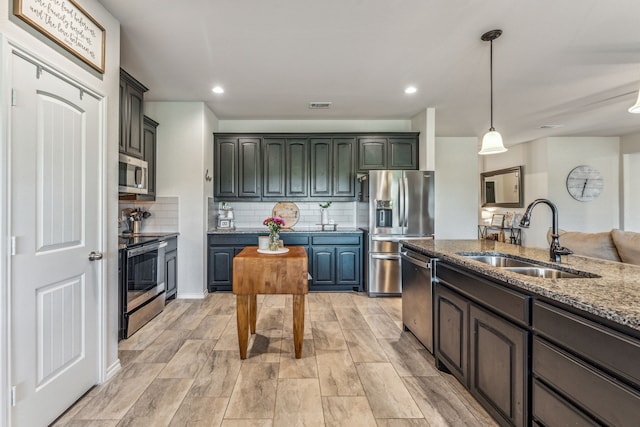 kitchen with decorative backsplash, appliances with stainless steel finishes, dark stone counters, sink, and hanging light fixtures