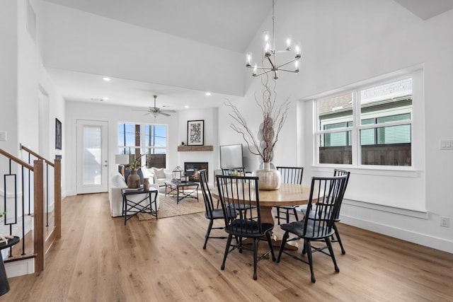 dining room featuring ceiling fan with notable chandelier, light hardwood / wood-style floors, and high vaulted ceiling