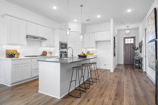 kitchen with built in microwave, a kitchen island with sink, pendant lighting, hardwood / wood-style floors, and white cabinetry