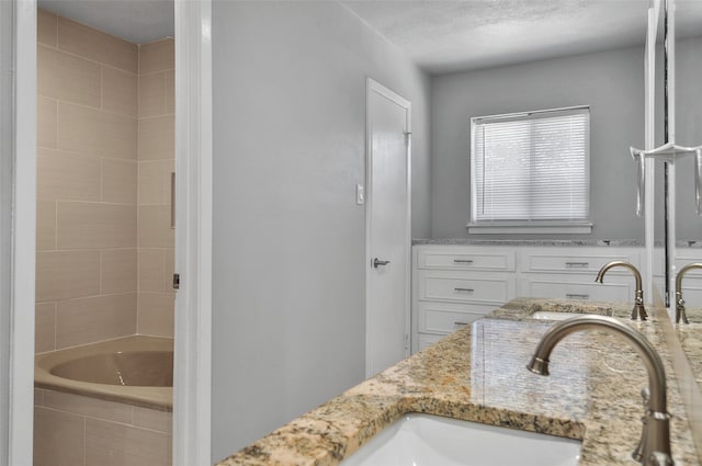 bathroom featuring a textured ceiling, vanity, and tiled tub