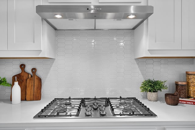 kitchen with tasteful backsplash, white cabinetry, range hood, and stainless steel gas cooktop