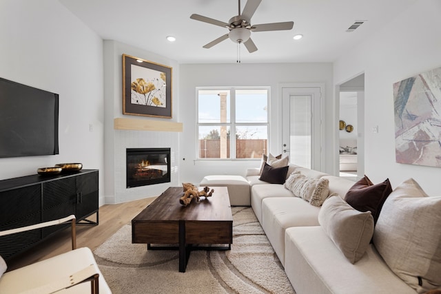 living room featuring ceiling fan, a fireplace, and light hardwood / wood-style flooring