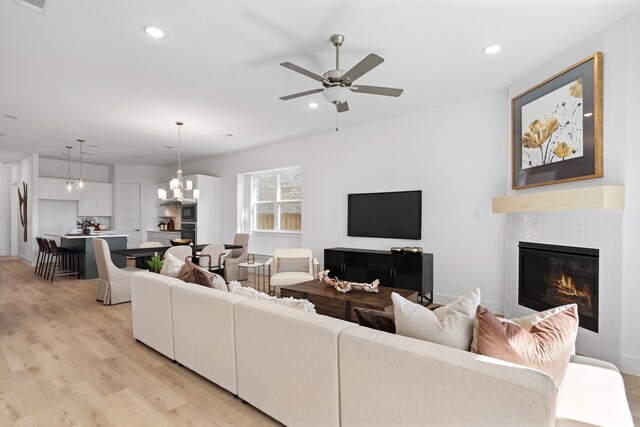 living room with a tile fireplace, ceiling fan with notable chandelier, and light wood-type flooring