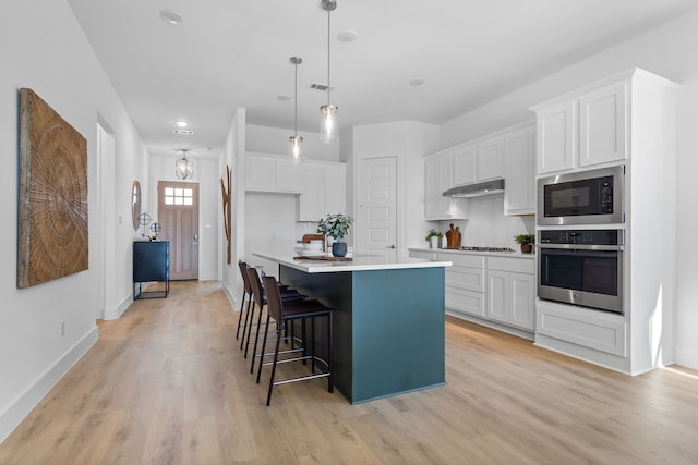 kitchen with white cabinetry, light hardwood / wood-style floors, decorative light fixtures, a kitchen island with sink, and appliances with stainless steel finishes