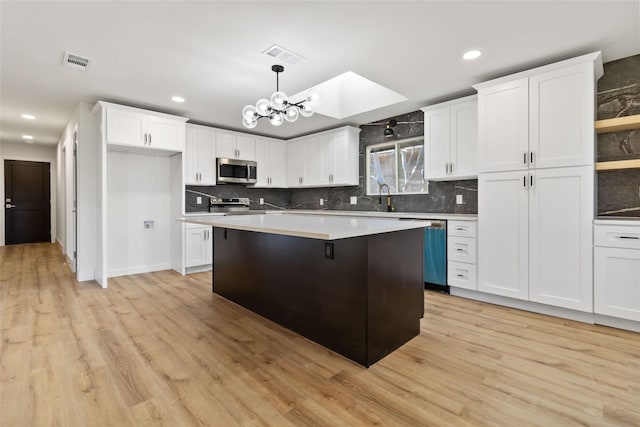 kitchen featuring pendant lighting, white cabinets, stainless steel appliances, and light hardwood / wood-style floors