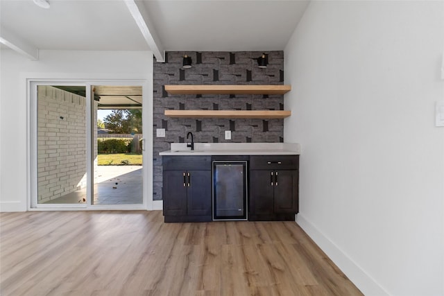 bar featuring dark brown cabinetry, light hardwood / wood-style flooring, beamed ceiling, and sink