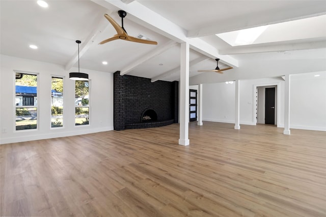 unfurnished living room with vaulted ceiling with skylight, ceiling fan, light wood-type flooring, and a brick fireplace