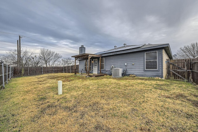 back of house featuring a lawn, central AC unit, and solar panels