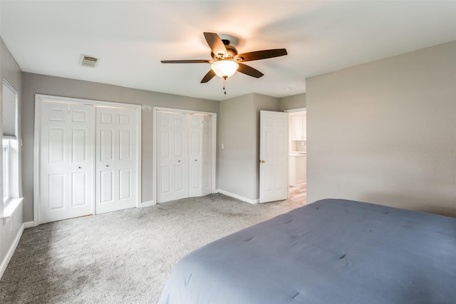 unfurnished bedroom featuring ceiling fan, carpet floors, and two closets