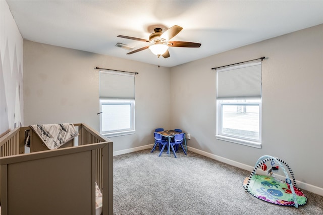 carpeted bedroom with multiple windows, a nursery area, and ceiling fan