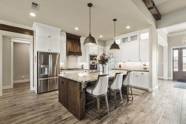 kitchen with white cabinets, stainless steel appliances, custom range hood, a center island with sink, and light hardwood / wood-style flooring