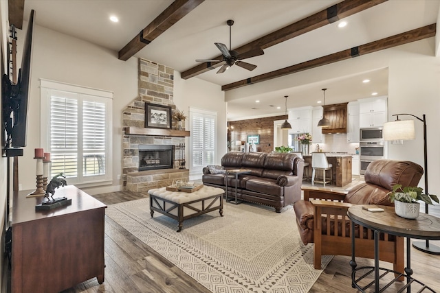 living room with beamed ceiling, a stone fireplace, hardwood / wood-style floors, and ceiling fan