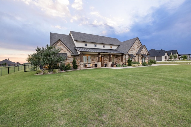 back of property at dusk featuring a standing seam roof, fence, metal roof, and a lawn