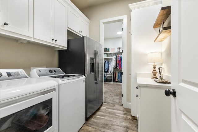 washroom featuring cabinets, washing machine and dryer, and light hardwood / wood-style flooring