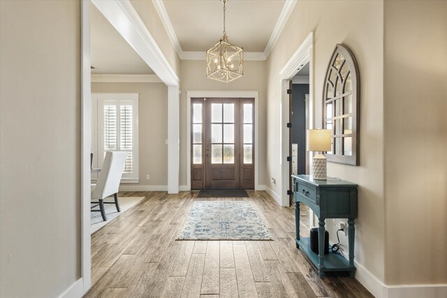 foyer with crown molding, hardwood / wood-style floors, and an inviting chandelier