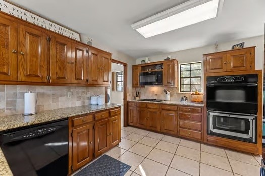 kitchen with light tile patterned floors, backsplash, light stone counters, and black appliances