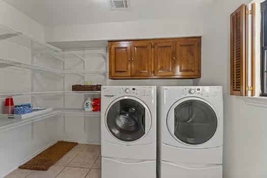 clothes washing area with cabinets, separate washer and dryer, and light tile patterned floors