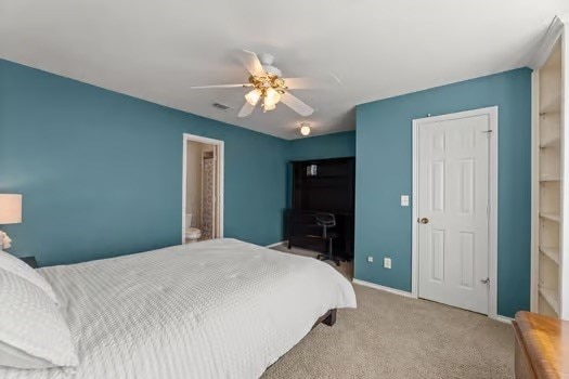 bedroom with ceiling fan, light colored carpet, and ensuite bath