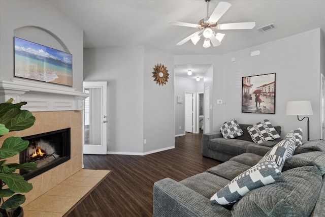 living room with dark hardwood / wood-style flooring, ceiling fan, and a tiled fireplace