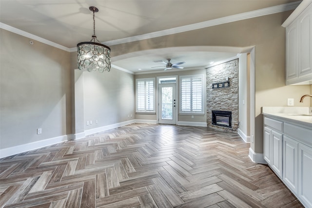 unfurnished living room featuring ceiling fan with notable chandelier, crown molding, a fireplace, and light parquet floors