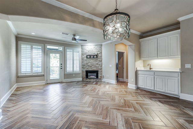 unfurnished living room featuring light parquet floors, ceiling fan with notable chandelier, a stone fireplace, sink, and crown molding