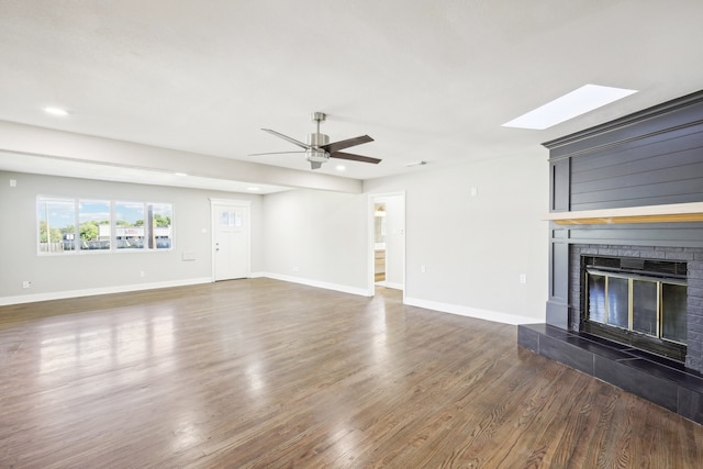 unfurnished living room with ceiling fan, dark hardwood / wood-style flooring, a fireplace, and a skylight