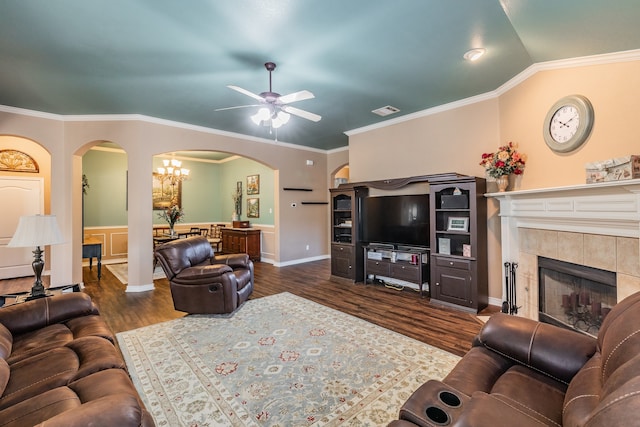 living room featuring dark hardwood / wood-style flooring, crown molding, lofted ceiling, a tiled fireplace, and ceiling fan with notable chandelier