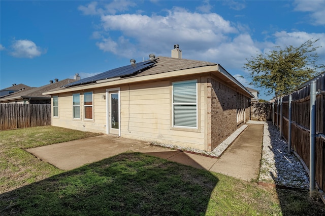 back of property with solar panels, a patio area, and a lawn