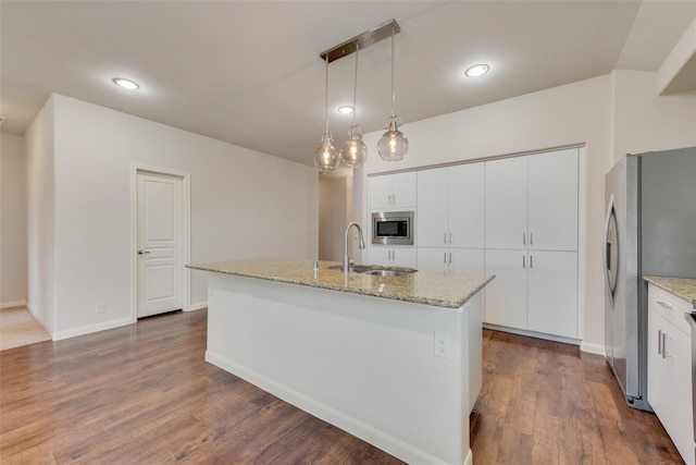 kitchen with white cabinetry, dark wood-type flooring, stainless steel appliances, pendant lighting, and a kitchen island with sink