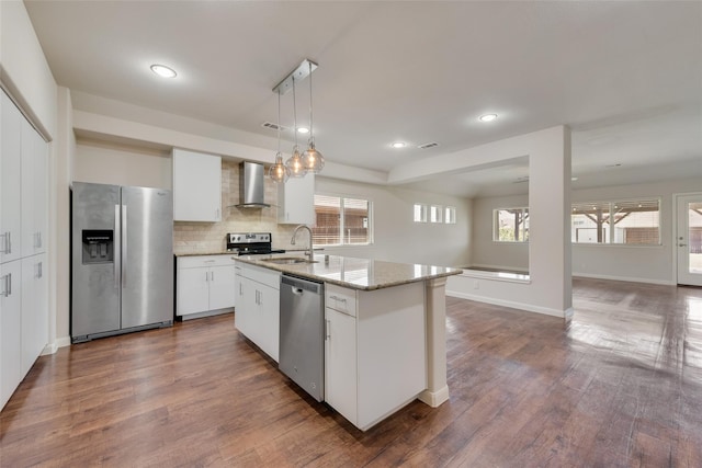 kitchen featuring appliances with stainless steel finishes, wall chimney exhaust hood, a kitchen island with sink, white cabinets, and dark hardwood / wood-style floors