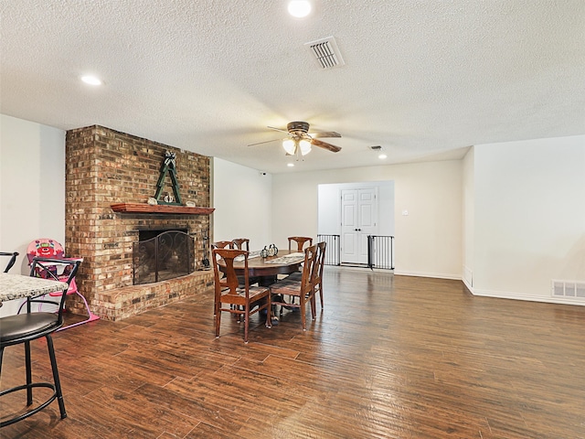 dining space with dark hardwood / wood-style flooring, a textured ceiling, and a brick fireplace