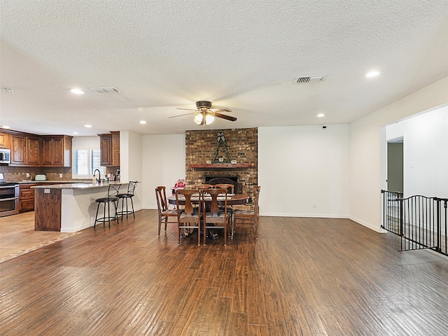 dining space featuring a textured ceiling, ceiling fan, dark wood-type flooring, and a brick fireplace