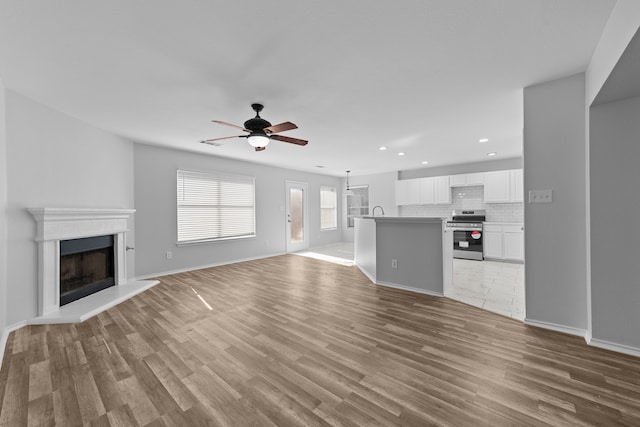 unfurnished living room with light hardwood / wood-style flooring, ceiling fan, and sink