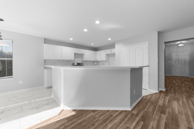 kitchen featuring white cabinetry, sink, tasteful backsplash, light hardwood / wood-style flooring, and an island with sink