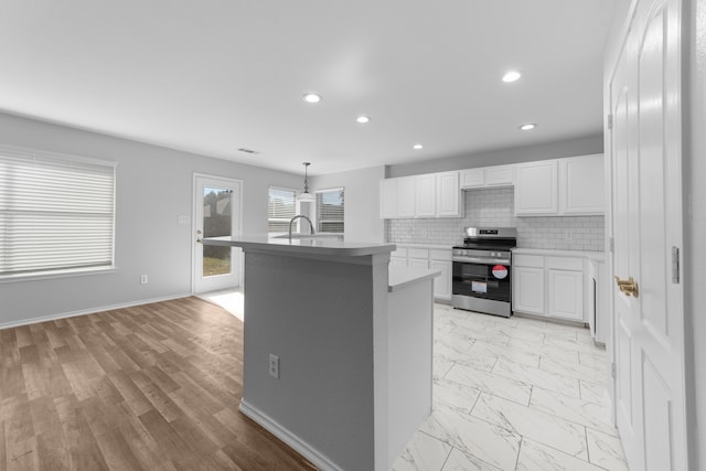 kitchen featuring white cabinetry, stainless steel range oven, an island with sink, decorative light fixtures, and decorative backsplash