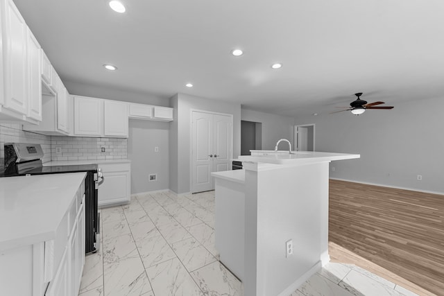 kitchen with stainless steel electric stove, white cabinets, backsplash, and an island with sink