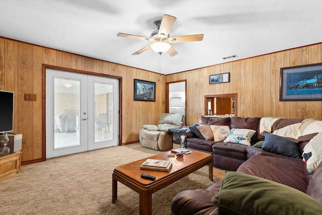 carpeted living room with french doors, ceiling fan, and wooden walls