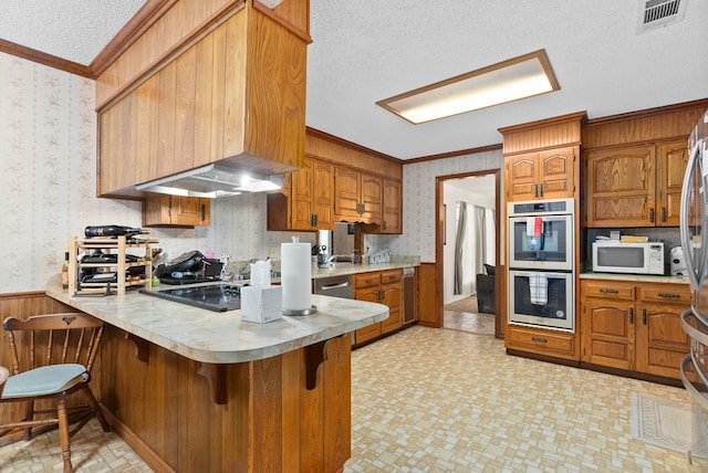 kitchen with kitchen peninsula, a kitchen breakfast bar, ornamental molding, a textured ceiling, and double oven