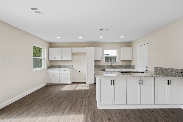 kitchen featuring white cabinets, kitchen peninsula, light stone countertops, and dark wood-type flooring