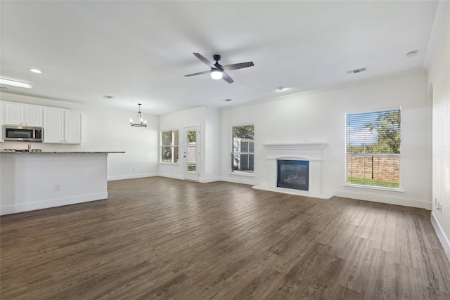 unfurnished living room with crown molding, ceiling fan with notable chandelier, and dark hardwood / wood-style floors