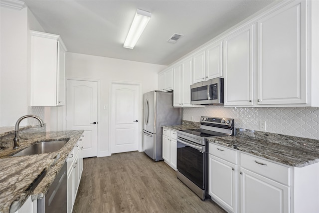 kitchen with white cabinets, dark stone countertops, light wood-type flooring, and stainless steel appliances