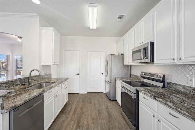 kitchen featuring dark stone counters, white cabinets, sink, light wood-type flooring, and stainless steel appliances