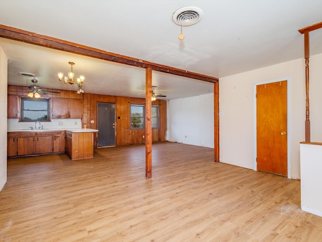 unfurnished living room with ceiling fan with notable chandelier, light wood-type flooring, wood walls, and sink