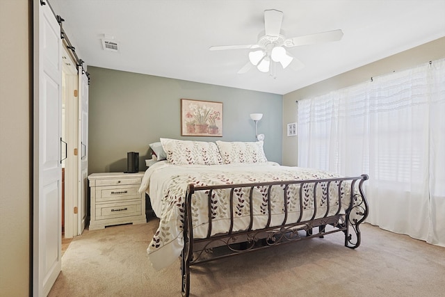 carpeted bedroom with ceiling fan and a barn door