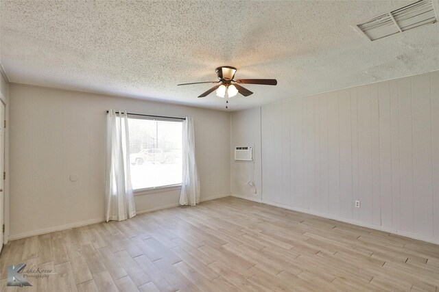 spare room with an AC wall unit, ceiling fan, light hardwood / wood-style floors, and a textured ceiling