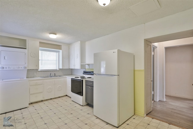 kitchen with decorative backsplash, a textured ceiling, white appliances, sink, and stacked washer and clothes dryer