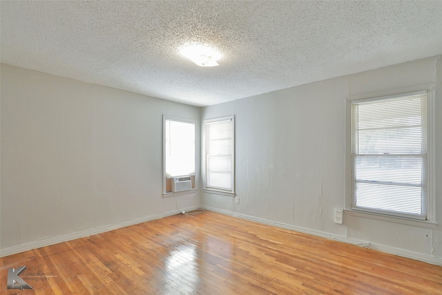 empty room with a textured ceiling, light hardwood / wood-style flooring, and cooling unit