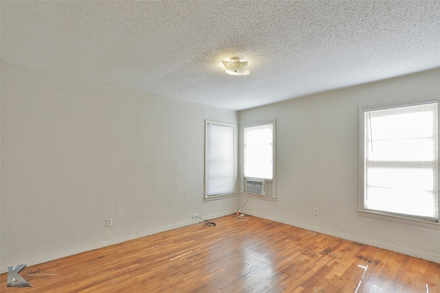 unfurnished room featuring cooling unit, wood-type flooring, and a textured ceiling