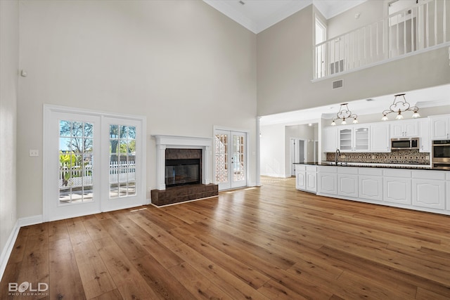 unfurnished living room featuring a towering ceiling, light hardwood / wood-style flooring, crown molding, and sink