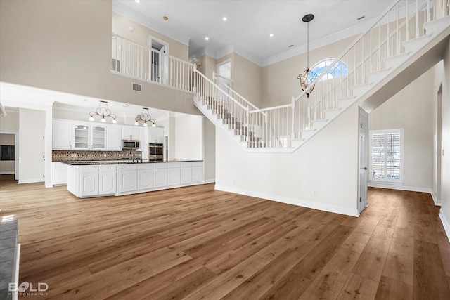 unfurnished living room with ornamental molding, light hardwood / wood-style flooring, a high ceiling, and a chandelier